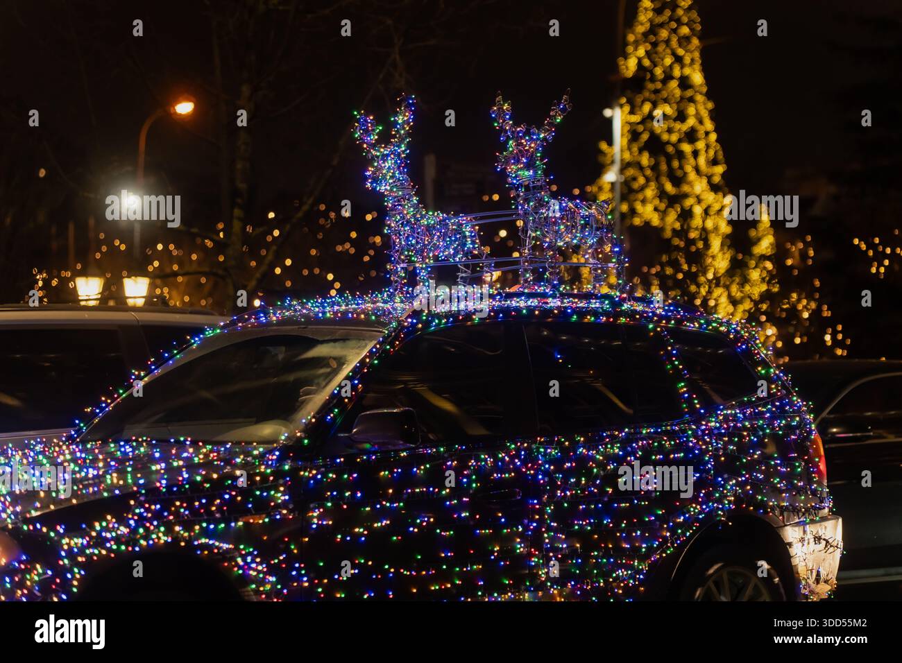 Voiture festive couverte de lumières de Noël colorées et de figures de renne illuminées sur le toit garé dans la rue de la ville la nuit créant un holi d'hiver joyeux Banque D'Images