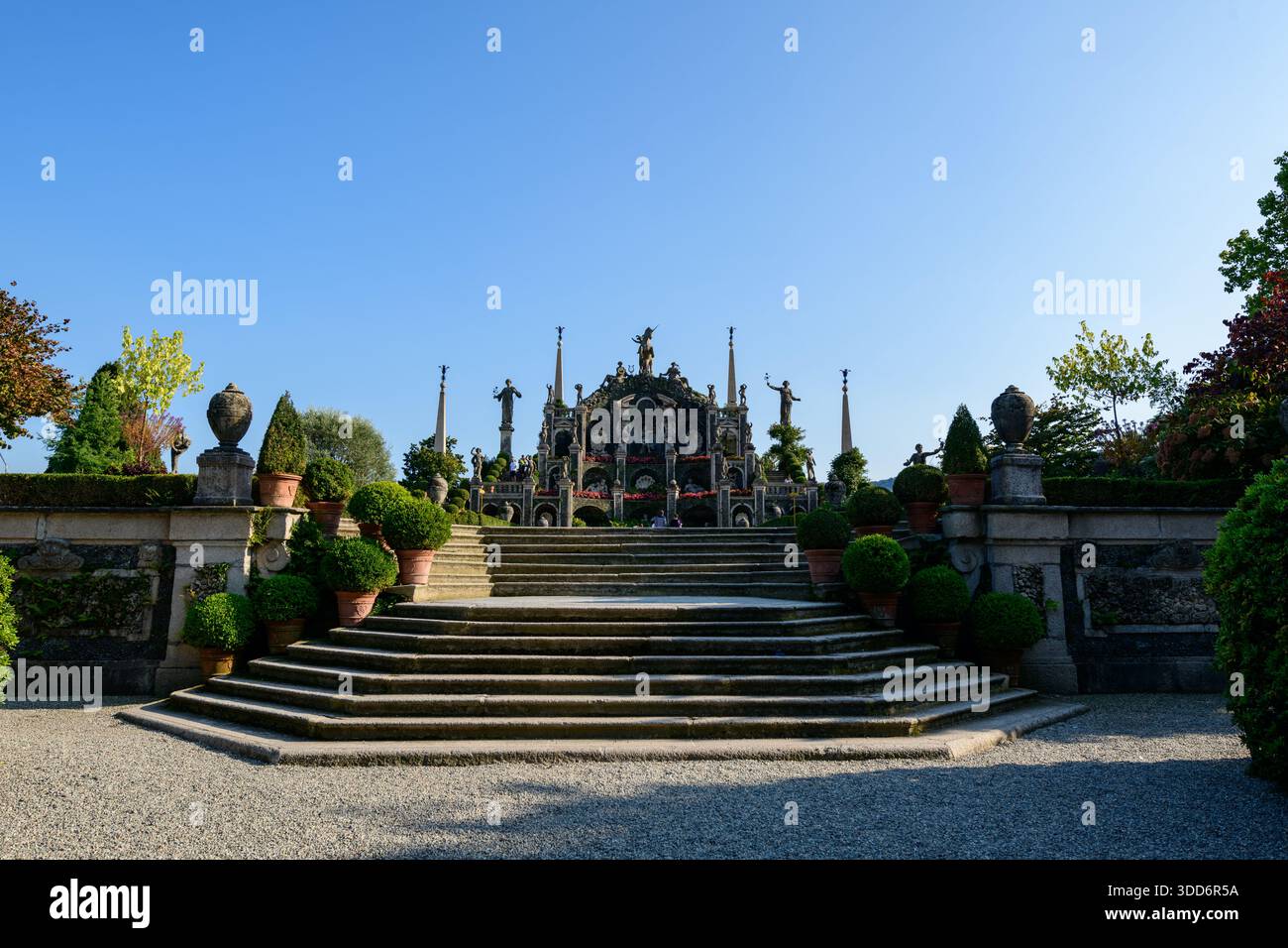 De larges marches en pierre mènent à une terrasse ornée de statues classiques et de verdure luxuriante dans les jardins Borroméens historiques. La lumière du soleil tôt le matin projette des ombres nettes, soulignant la symétrie et le design formel de ce monument italien. Banque D'Images