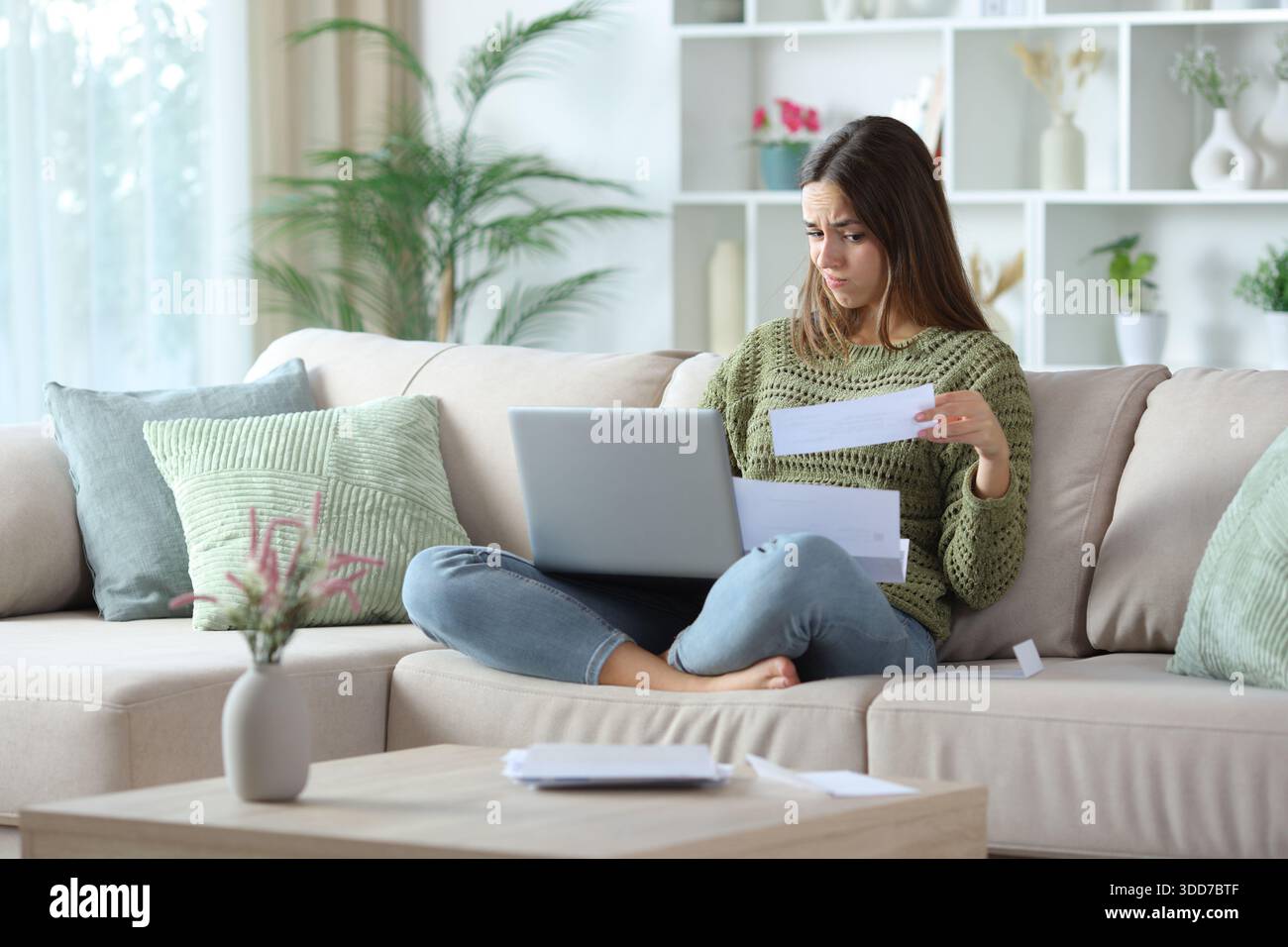 Femme confuse faisant de la comptabilité en ligne assise sur un canapé à la maison Banque D'Images