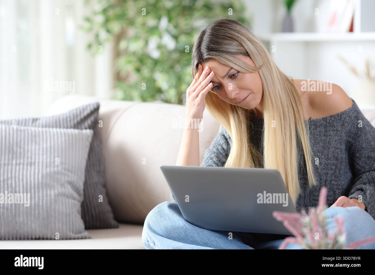 Femme se plaignant après erreur en vérifiant l'ordinateur portable assis sur un canapé à la maison Banque D'Images