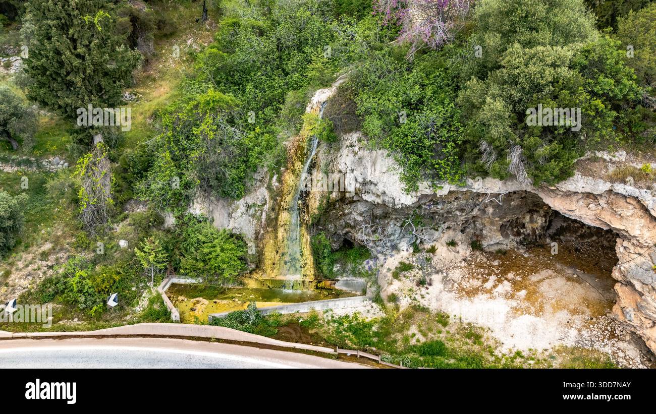 Vue aérienne d'une petite cascade naturelle coulant sur la roche calcaire à côté d'une route rurale à Elaiona, Grèce centrale, entourée d'une végétation verte an Banque D'Images