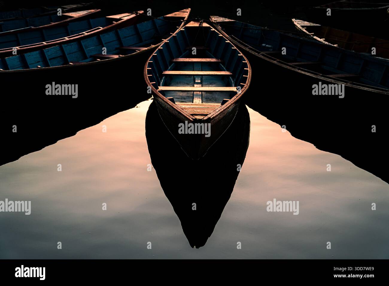 Une composition symétrique de bateaux à rames traditionnels en bois flottant sur de l'eau calme, créant un reflet semblable à un miroir. Banque D'Images