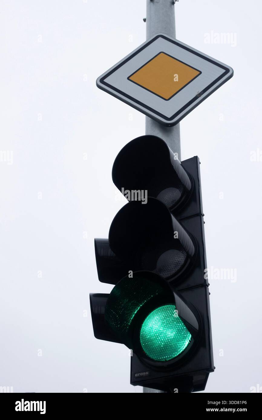 Feu vert allumé contre un ciel pâle, signalant l'autorisation de se rendre à une intersection urbaine Banque D'Images