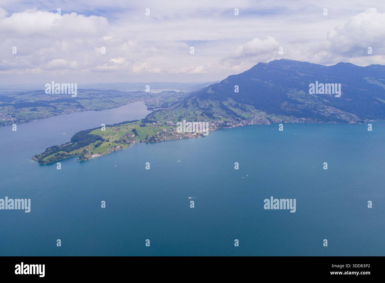 Vue aérienne d'un paysage vibrant où le lac bleu profond rencontre les collines verdoyantes, couronnées par une montagne majestueuse sous un ciel doux, Treptower par Banque D'Images