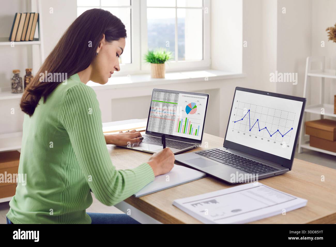 Femme d'affaires examinant des analyses et des graphiques sur deux ordinateurs portables au bureau Banque D'Images