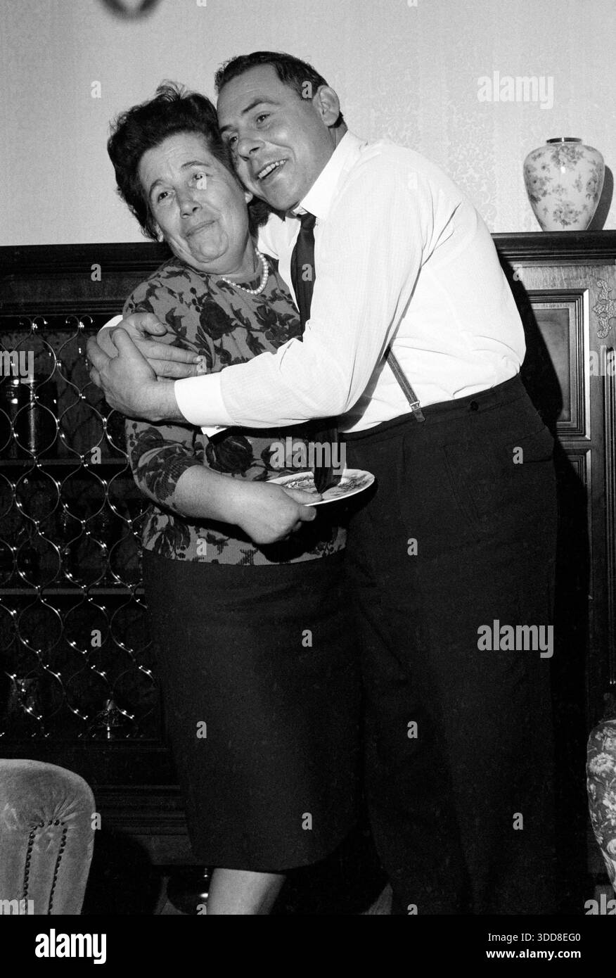 Sechzigerjahre, 12.11.1966, Deutschland, Menschen, Familienfeier, Fotoshooting, Frau und Mann, Frieda 50 - 55 Jahre wird von Menni 35 bis 40 Jahre umarmt und beide stehen im Wohnzimmer und haben Spass und lachen, Nahaufnahme Sechzigerjahre, 12.11.1966, Deutschland, Menschen, Familienfeier, Fotoshooting, Frau und Mann, Frieda 50 bis 55 Jahre mit Hochfrisur in Bluse und Rock wird von Menni 35 bis 40 Jahre kurzes Haar in Oberhemd mit Krawatte und Hosentraeger umarmt und beide stehen im Wohnzimmer und haben Spass und lachen, Nahaufnahme, années 60, 12.11.1966, Allemagne, personnes, fête de famille, ph Banque D'Images