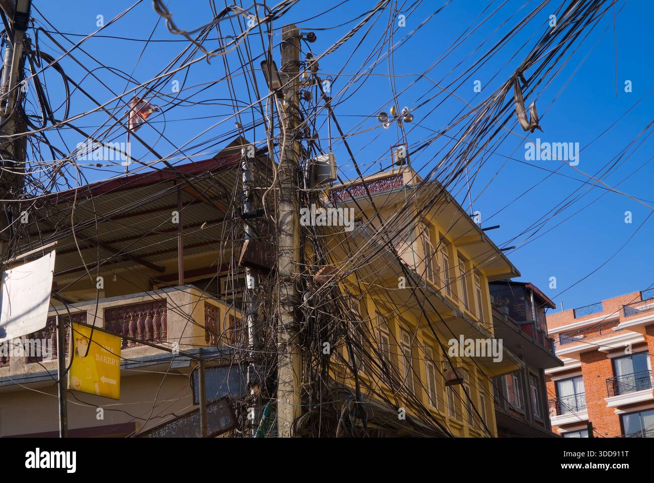 Poteau électrique urbain bondé de câbles électriques enchevêtrés devant un bâtiment sous un ciel bleu clair, mettant en évidence l'infrastructure dense de la ville. Banque D'Images