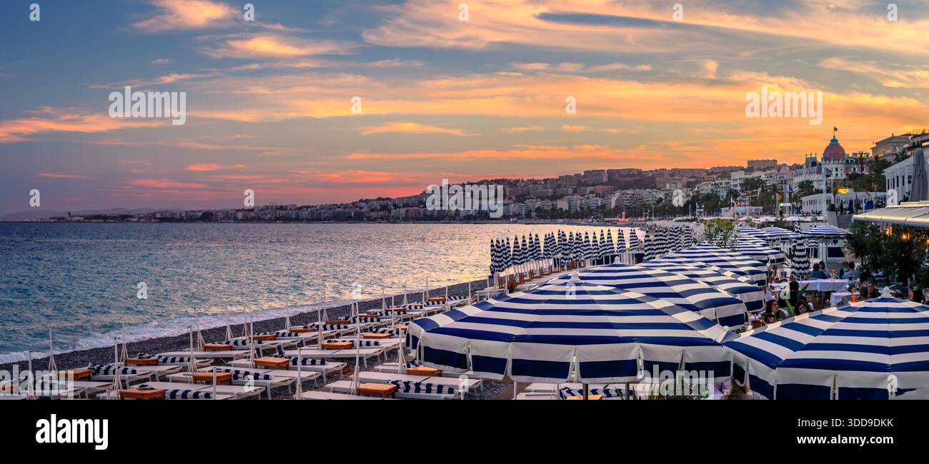 Parasols rayés bleus et blancs sur une plage de galets, panorama d'un coucher de soleil doré sur la mer Méditerranée le long de la Promenade des Anglais, Nice, France Banque D'Images