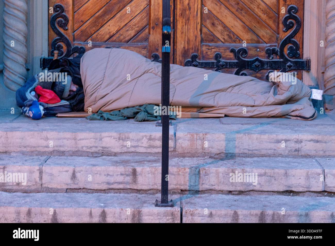 Toronto, ON, Canada - 15 octobre 2025 : personne sans-abri dormant dans un sac sur des marches de pierre froide près d'une porte, illustrant la pauvreté urbaine, marginalizati Banque D'Images