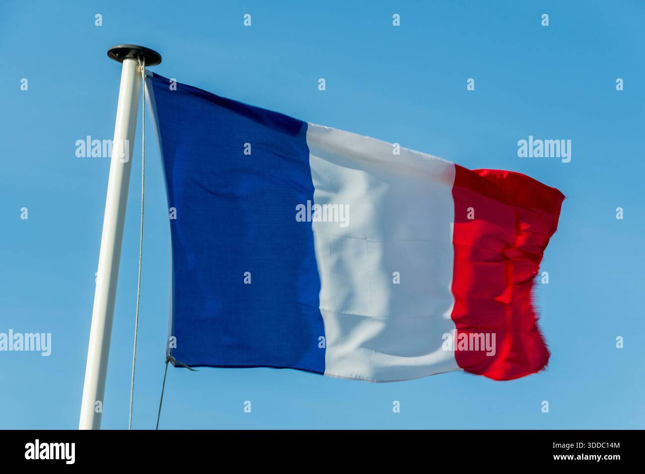 Un drapeau français bat dans le vent sur un mât de drapeau blanc. L'arrière-plan est un ciel clair et bleu Azur. Banque D'Images