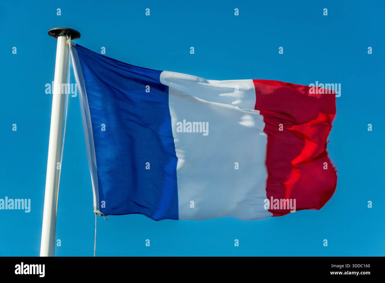 Un drapeau français bat dans le vent sur un mât de drapeau blanc. L'arrière-plan est un ciel clair et bleu Azur. Banque D'Images