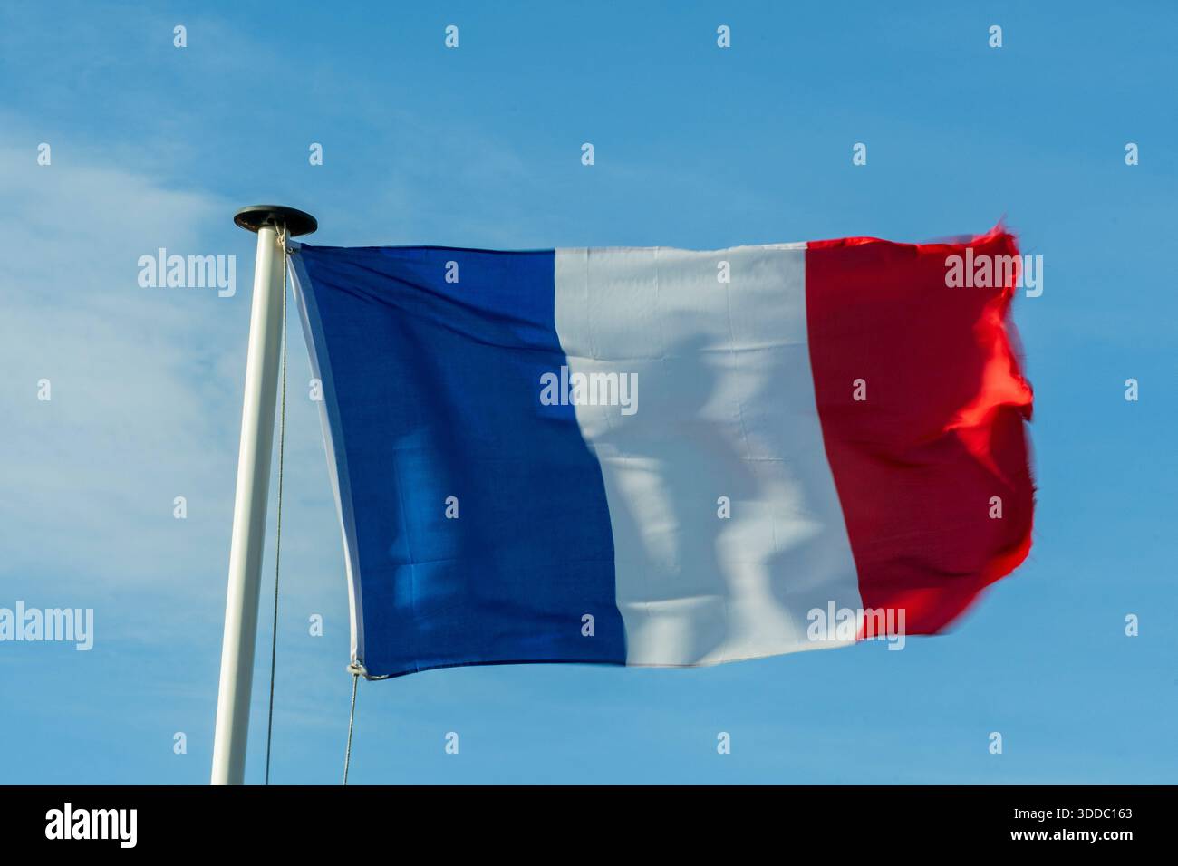 Un drapeau français bat dans le vent sur un mât de drapeau blanc. L'arrière-plan est un ciel clair et bleu Azur. Banque D'Images