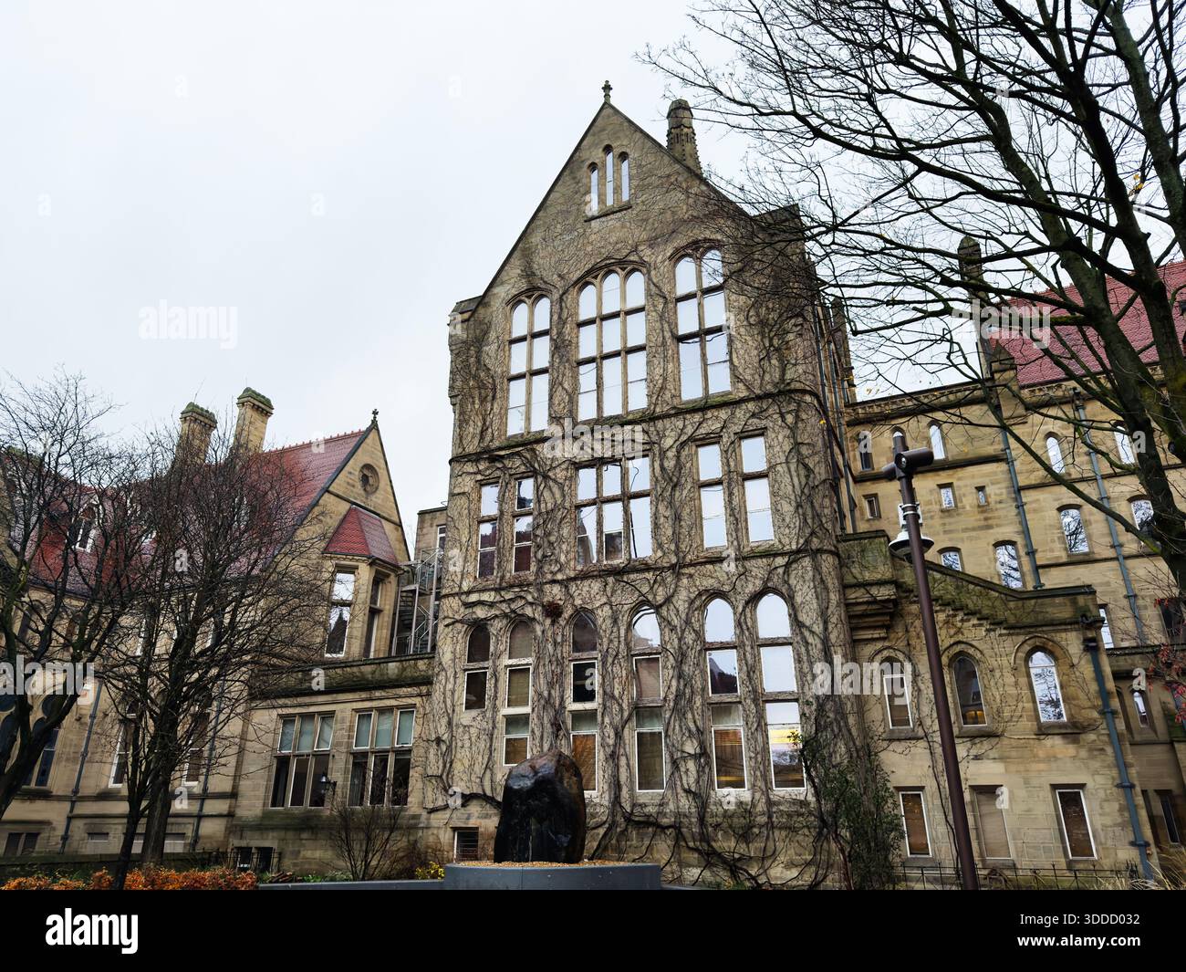 Manchester, Royaume-Uni - 06 décembre 2025 : bâtiment historique de Manchester avec du lierre sur des murs en pierre et de hautes fenêtres cintrées. Banque D'Images