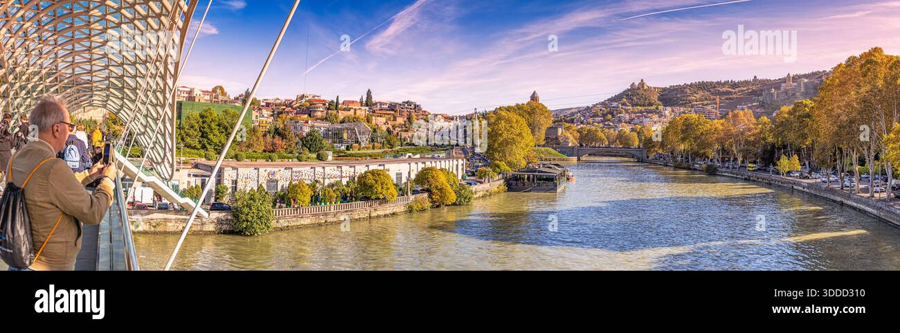 31 octobre 2025, Tbilissi, Géorgie : touristes explorant l'architecture moderne sur le pont de la paix surplombant la rivière Kura et le paysage urbain historique de Tbilissi Banque D'Images
