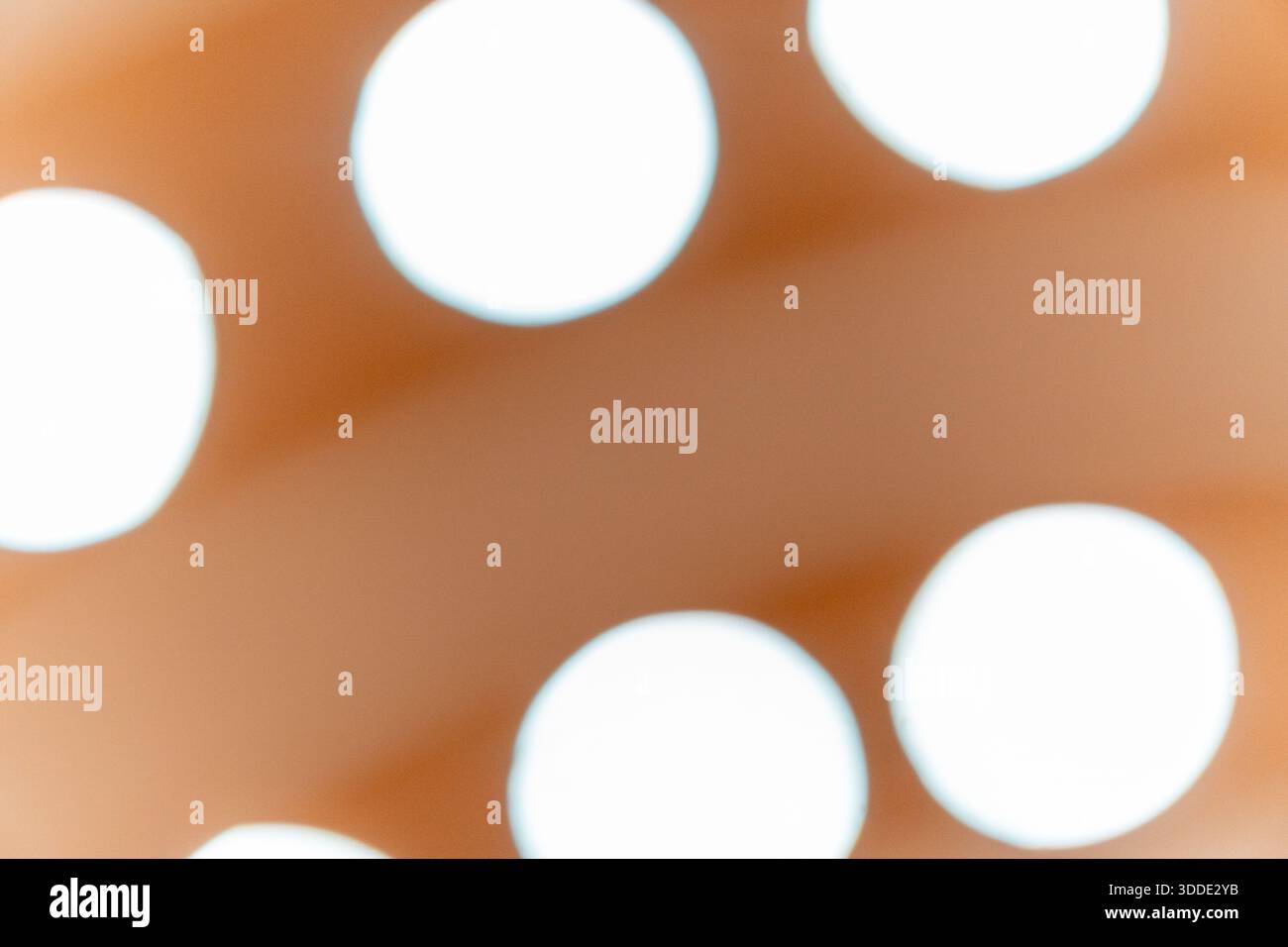 Un fond abstrait doux et flou avec des taches de bokeh circulaires blanches brillantes sur une surface orange et marron chaude. Banque D'Images
