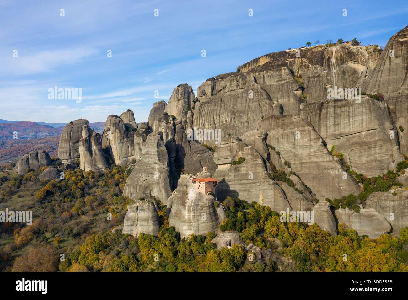 Le monastère d'Agios Nikolaos s'accroche de façon spectaculaire aux falaises abruptes de grès au-dessus d'une forêt colorée d'automne dans les Météores, en Grèce. Les formations rocheuses accidentées et le ciel étendu créent un paysage saisissant et serein. Banque D'Images