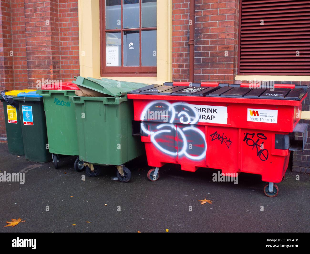 Rangée de poubelles commerciales et grande benne industrielle rouge avec des étiquettes graffiti alignées contre un mur de briques Banque D'Images