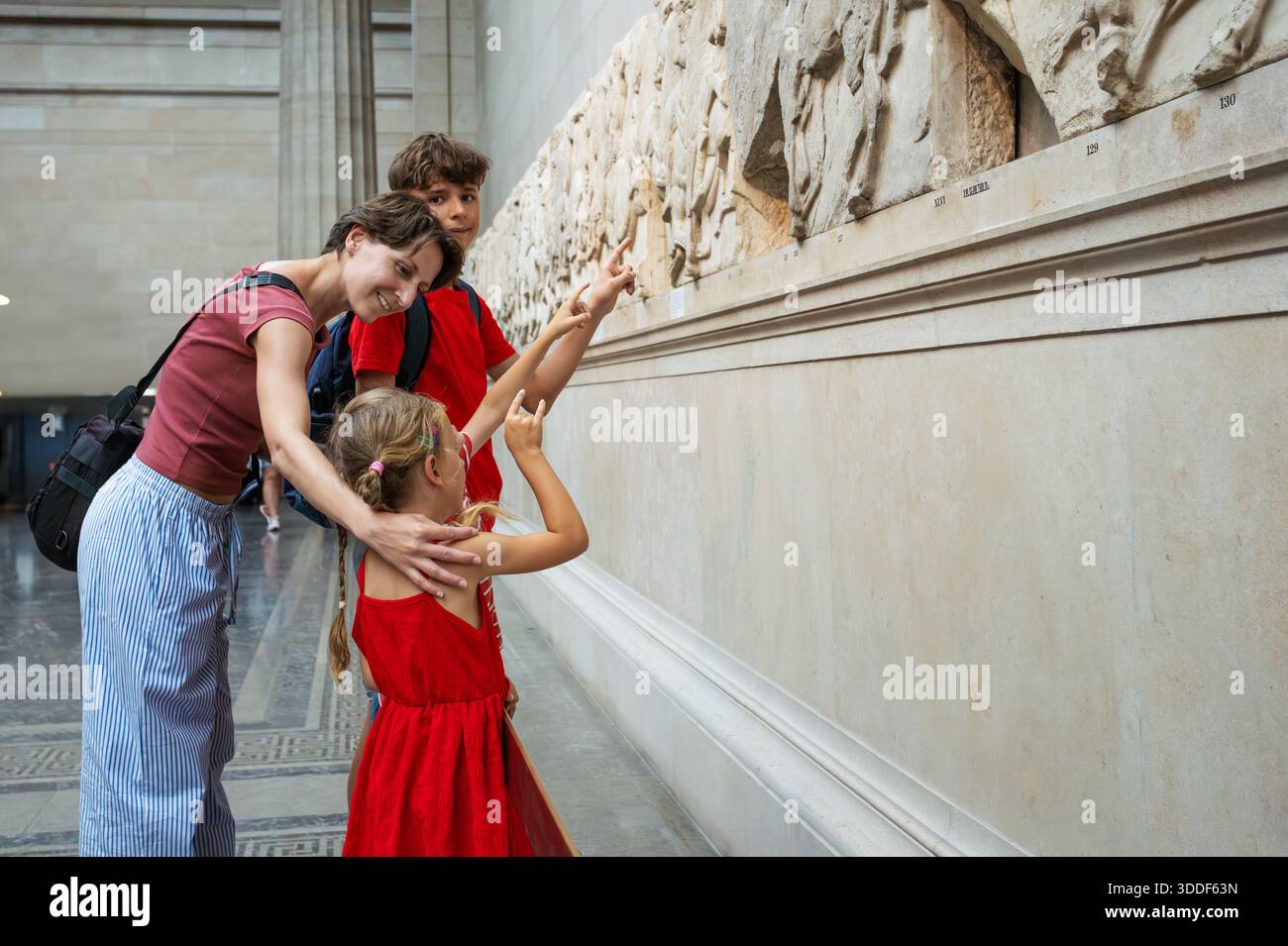 Un groupe d'enfants et leurs parents se tiennent captivés par une sculpture sur pierre exposée dans une salle d'exposition Banque D'Images