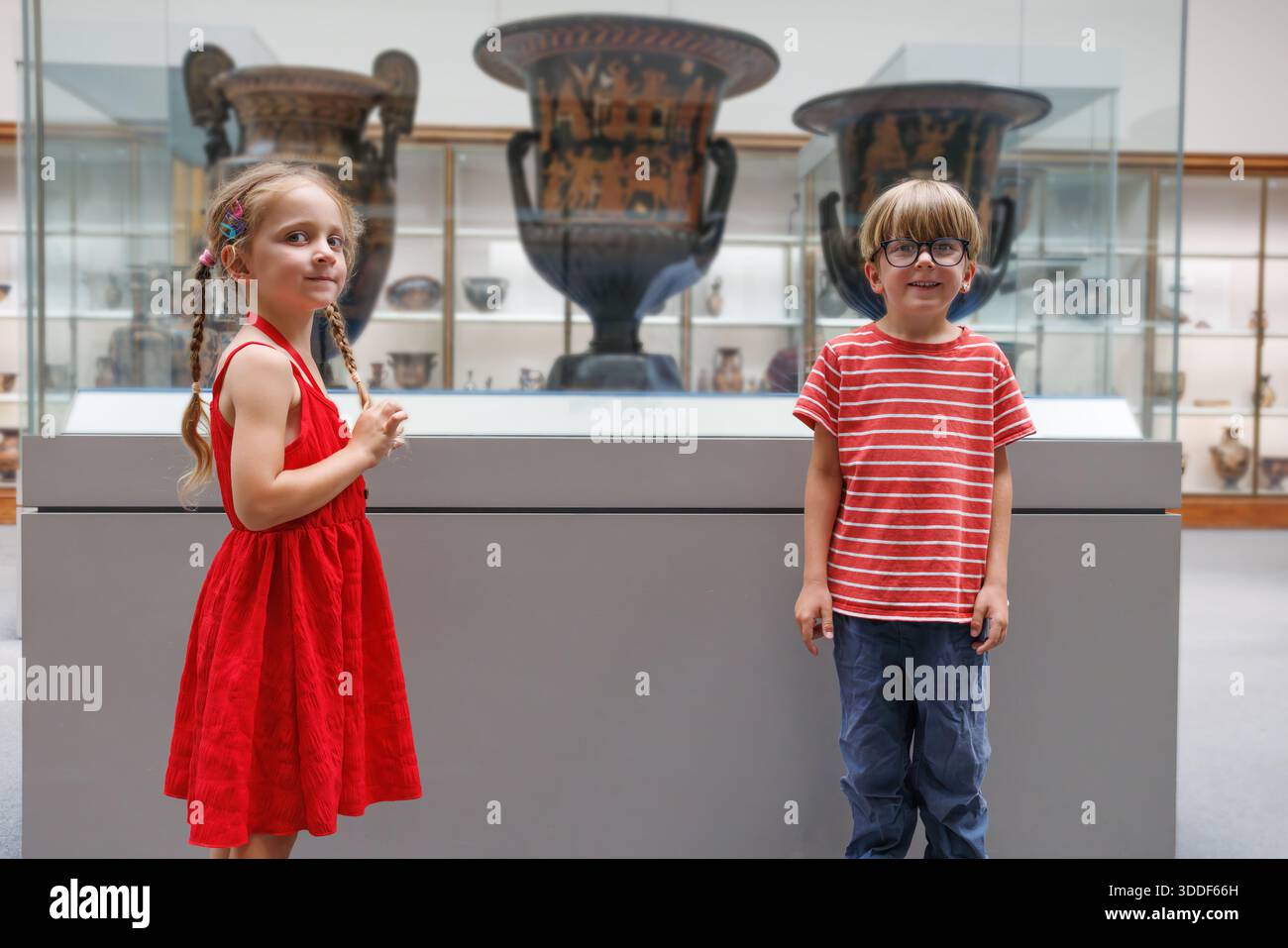 Une paire d'enfants contemplent d'impressionnantes vieilles urnes dans une vitrine, entourées de divers artefacts dans une galerie Banque D'Images