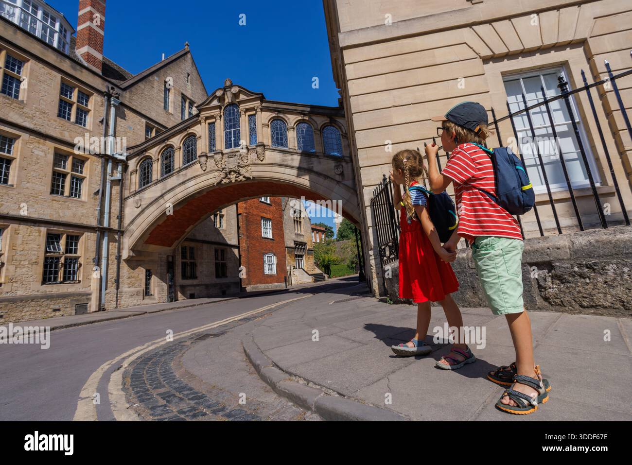 Deux enfants, explorant une rue historique de la ville contemplent l'emblématique Bridge of Soupirs reliant de vieux bâtiments, Oxford, Royaume-Uni Banque D'Images