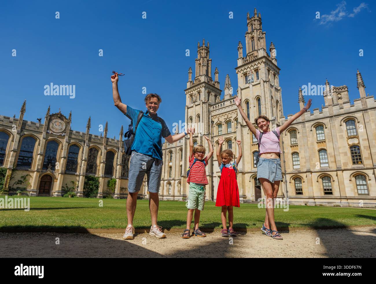 Une famille de quatre personnes se tient joyeusement avec les bras levés devant un grand bâtiment historique All Souls College sous un ciel bleu vif Banque D'Images