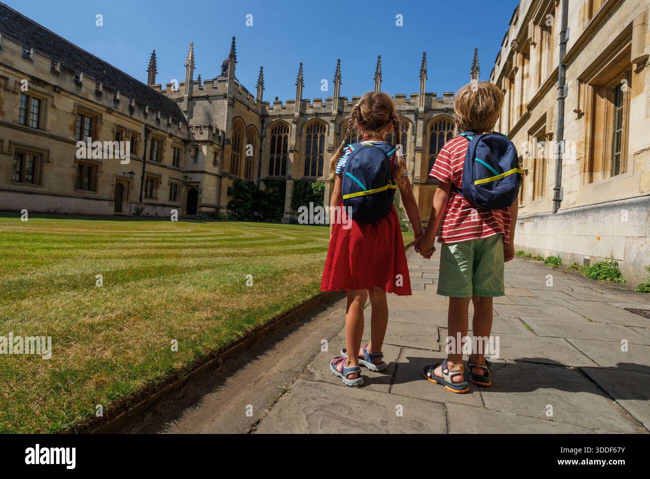 Par une journée ensoleillée, deux enfants se tiennent la main et équipés de sacs à dos se tiennent devant une structure vénérable de All Souls College, Oxford, Grande-Bretagne Banque D'Images
