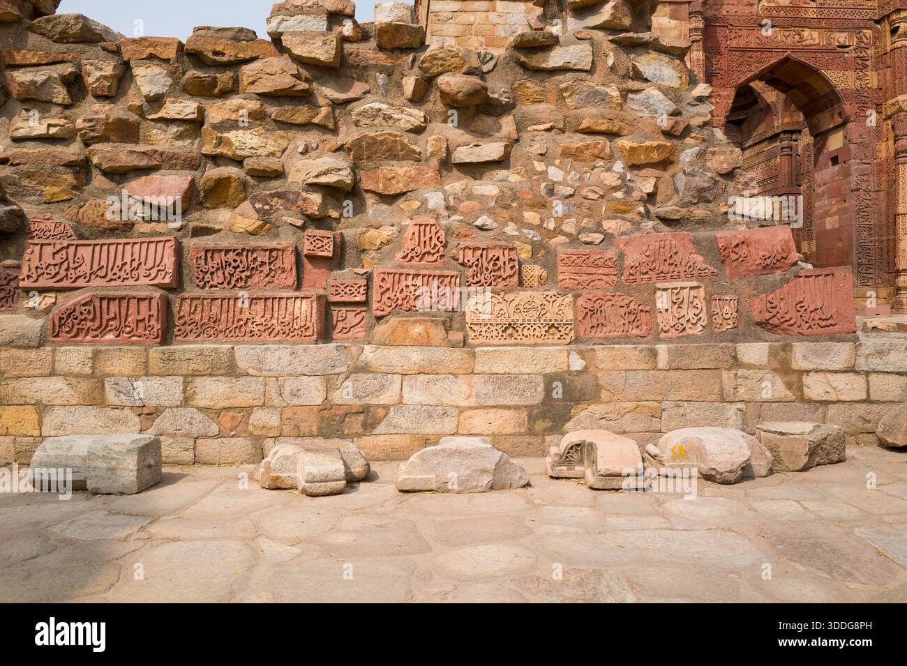 Mur historique fragmenté avec des blocs de grès sculptés avec des inscriptions calligraphiques complexes et des dessins géométriques au complexe Qutub Minar à Delhi. La lumière chaude du jour révèle la maçonnerie texturée et les surfaces altérées. Banque D'Images