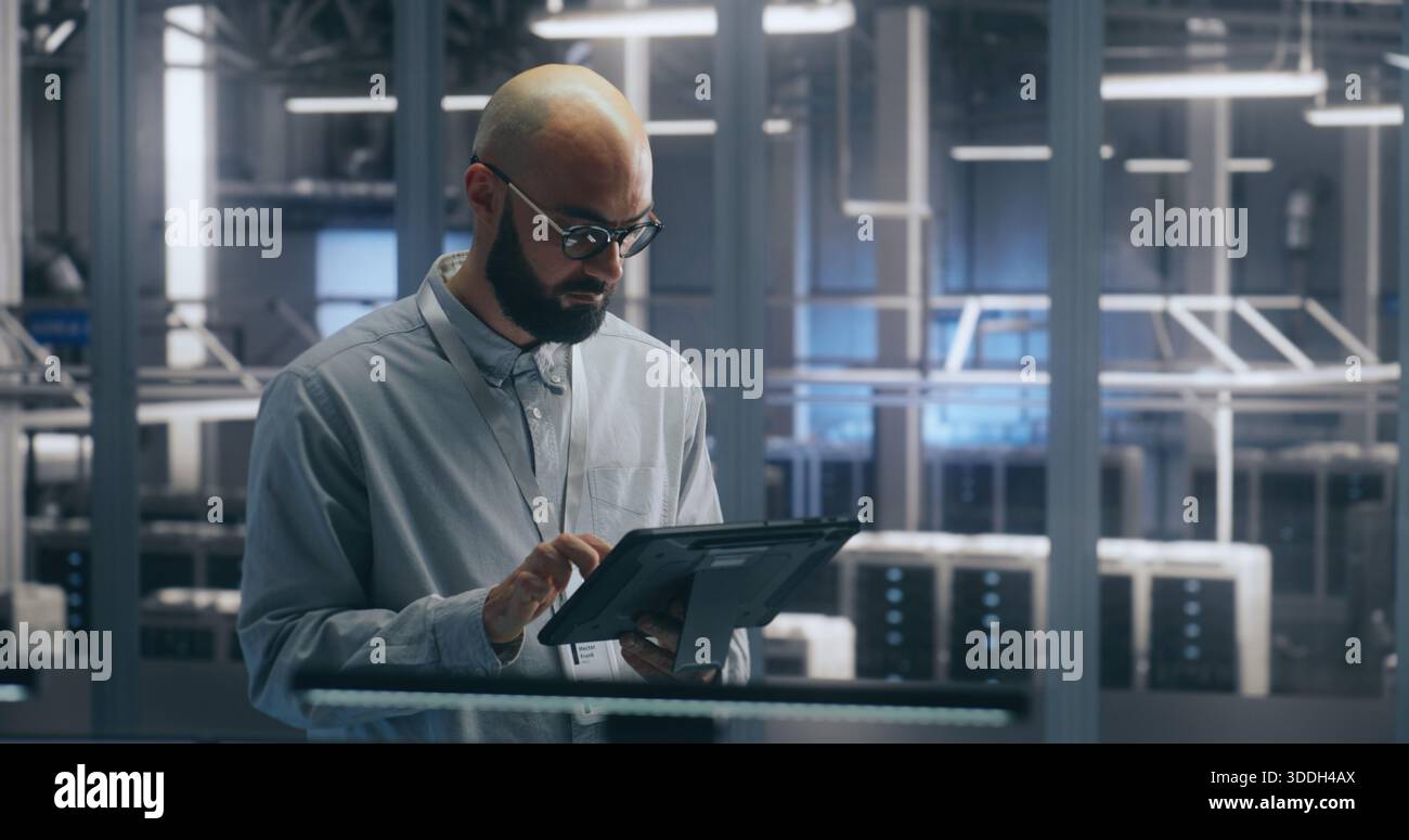 Technicien utilisant une tablette pour la gestion des actifs dans un datacenter. Man Check Assets dans le hall des serveurs. Une collègue marche en arrière-plan. Concept de gestion interactive des actifs et de workflow INFORMATIQUE. Banque D'Images