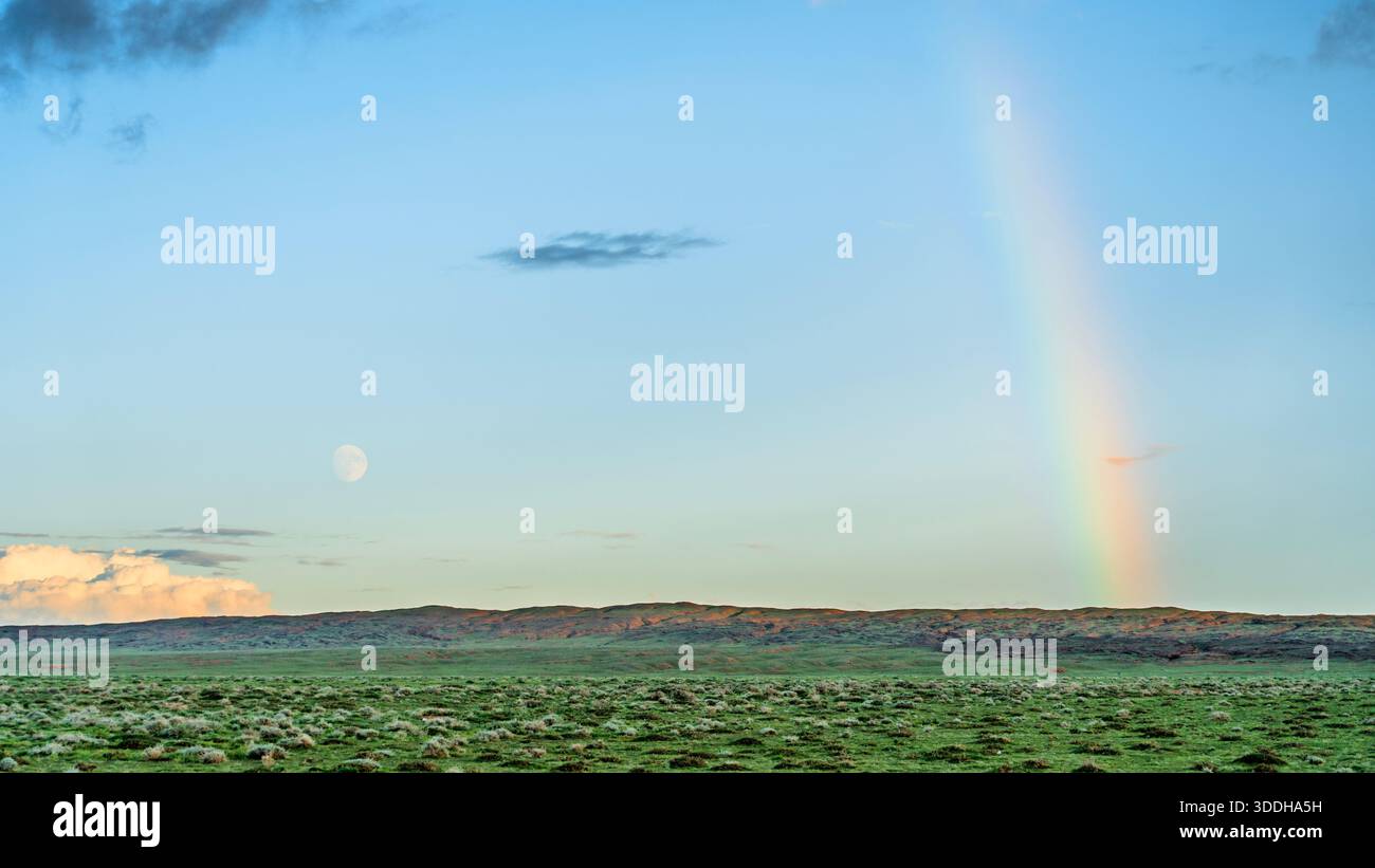 Arc-en-ciel et lune sur un paysage de steppe verdoyant au coucher du soleil Banque D'Images