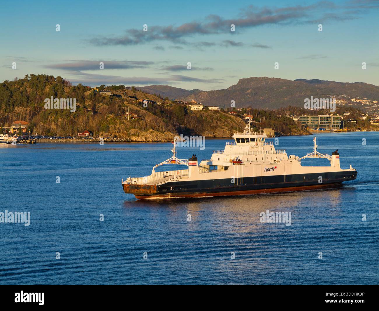 Bergen, Norvège - novembre 25 2025 : un ferry de voiture navigue à travers le fjord bleu de Bergen, Norvège, avec des maisons à flanc de colline et des montagnes sous la douce lumière automnale. Banque D'Images