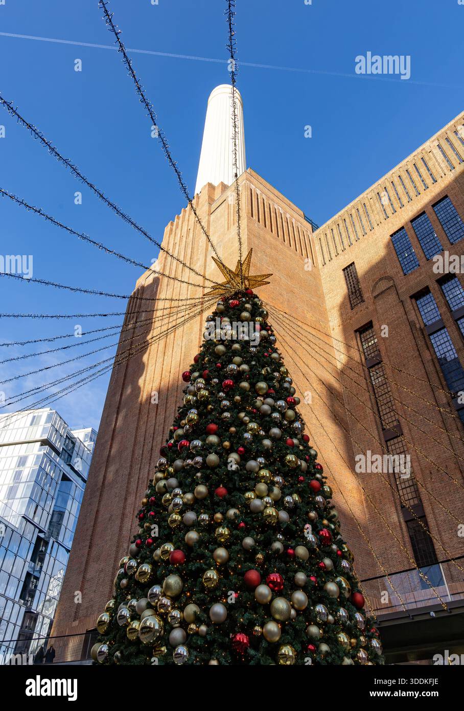 Grand arbre de Noël décoré avec des lumières festives devant le bâtiment de la centrale électrique de Battersea avec une cheminée blanche un jour de ciel bleu clair Banque D'Images