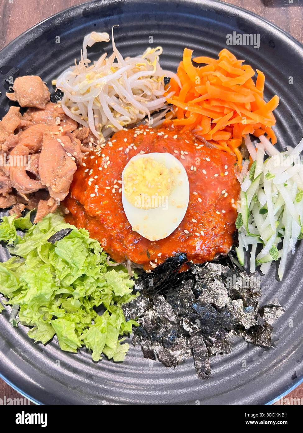 Coréen Bibimbap Cold Noodle style en vertical, œuf à moitié bouillant pondu sur le dessus de la sauce. Banque D'Images