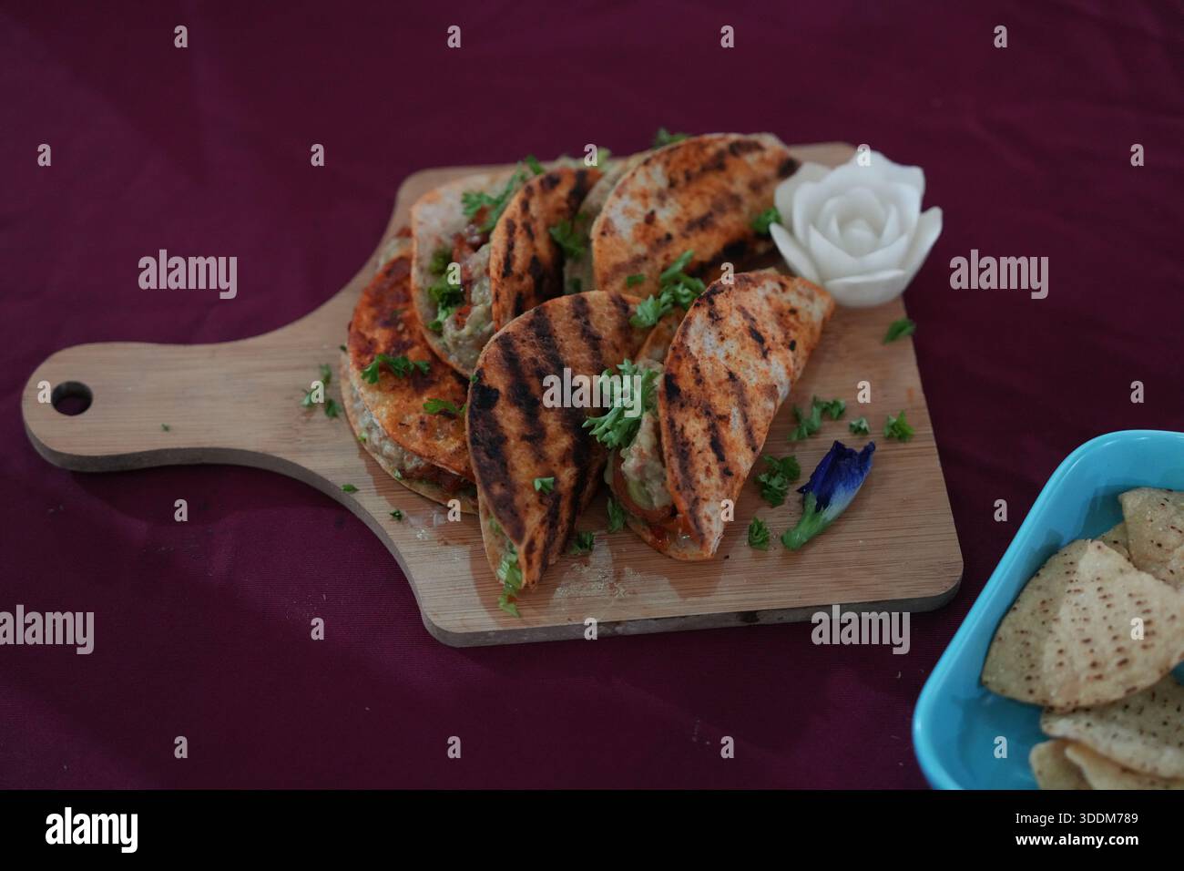 Une portion de tacos au poulet grillé sur une planche de bois rustique, garnie de coriandre et servie avec un côté de chips de tortilla croustillantes. Banque D'Images