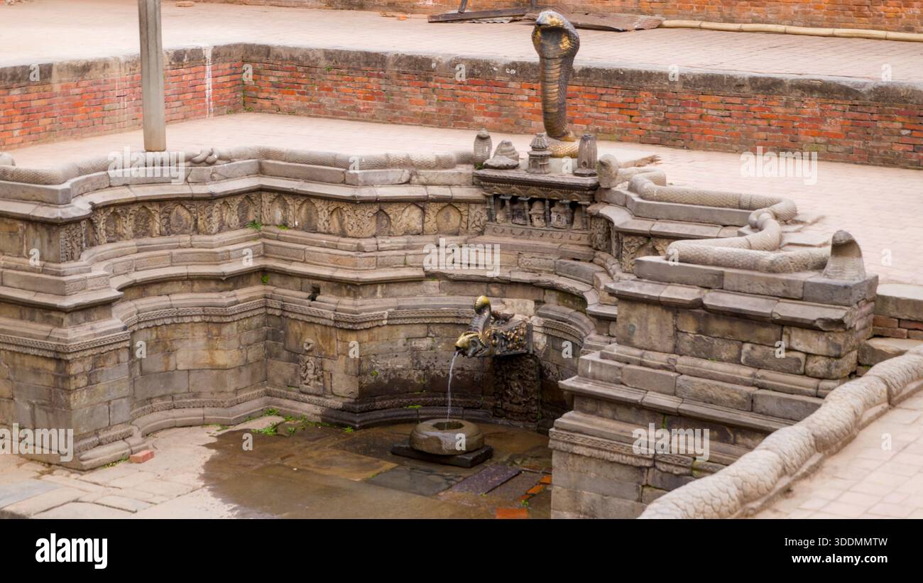 L'ancienne fontaine en pierre présente une sculpture de cobra avec de l'eau qui coule, entourée d'un mur de briques et de détails historiques. Banque D'Images