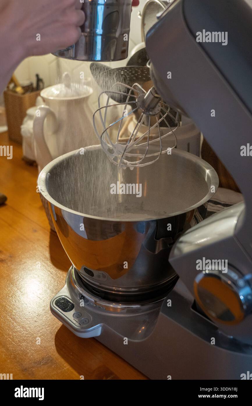 Les mains tamisent la farine dans le bol du mélangeur tout en préparant la pâte charlotte aux pommes sur le comptoir de cuisine en bois, capturant le moment de cuisson à la maison Banque D'Images