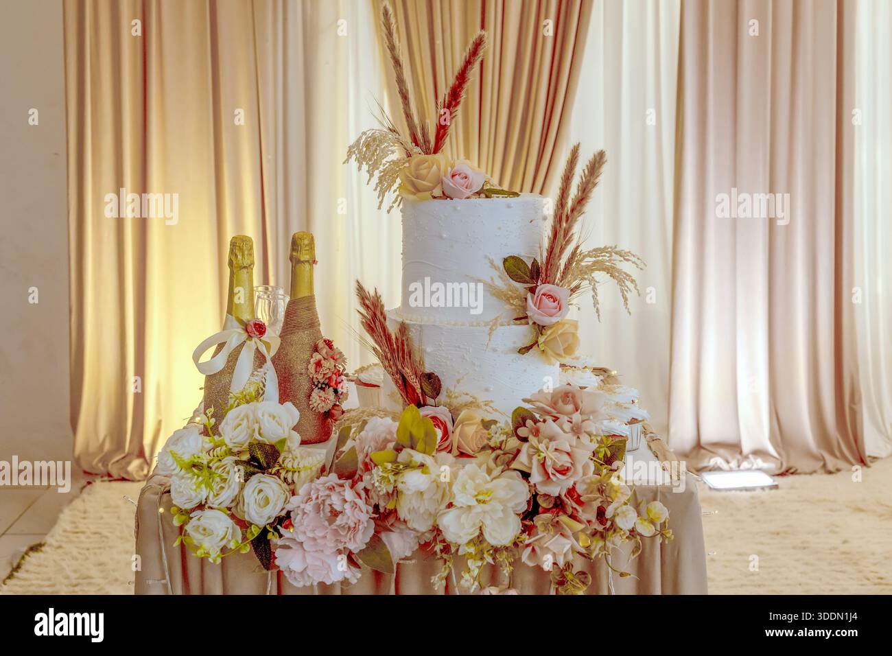 Élégant gâteau de mariage blanc avec bouteilles de champagne et décorations florales Banque D'Images