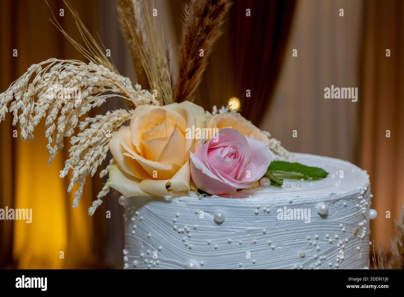 Élégant gâteau blanc orné de roses délicates et d'accents floraux séchés naturels Banque D'Images