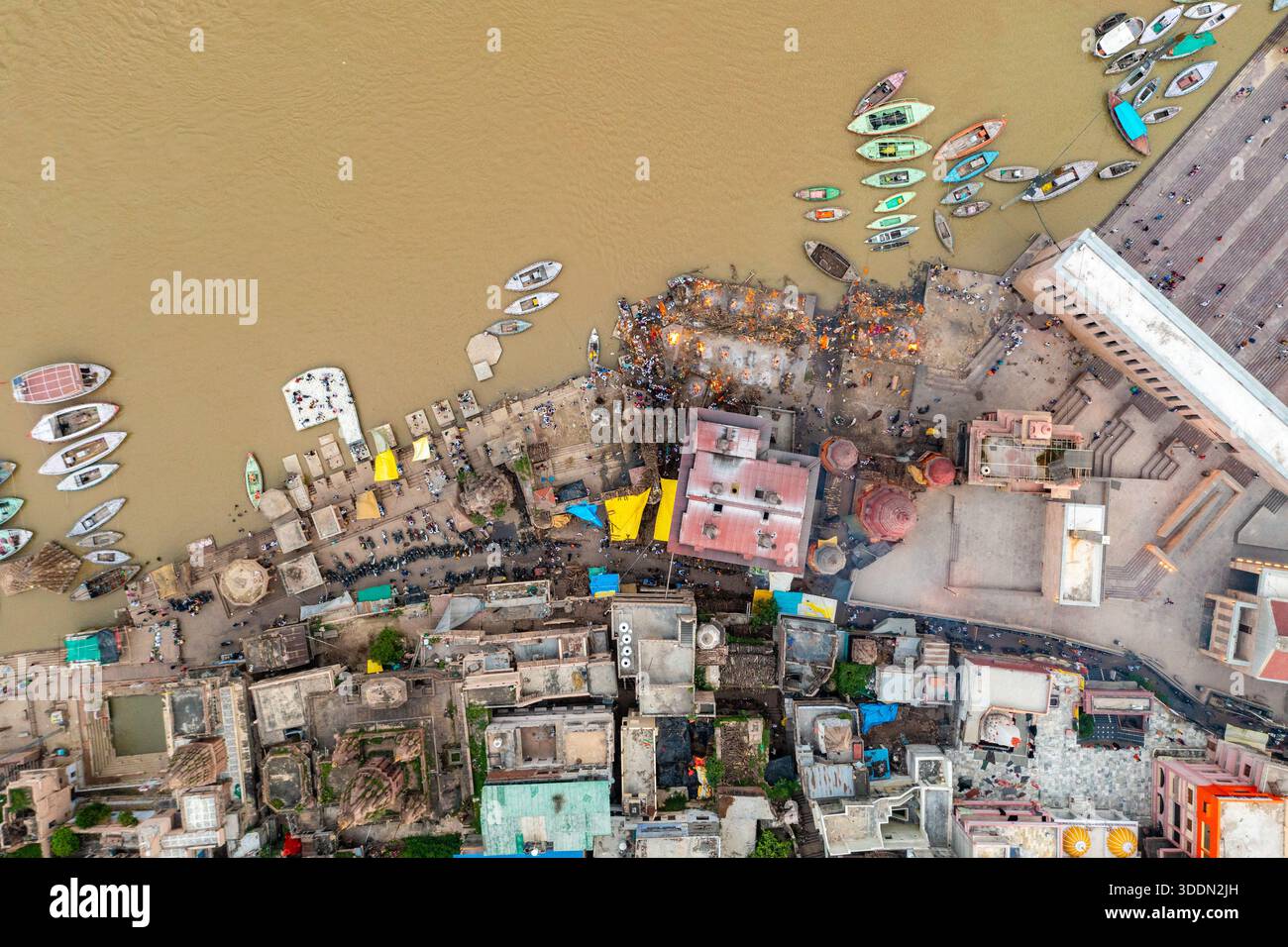 Vue aérienne de la rivière ocre embrasse des ghats bordés de bateaux et de bâtiments, où la vie et la mort se mêlent dans une danse sacrée, Varanasi, Uttar Pradesh, Banque D'Images