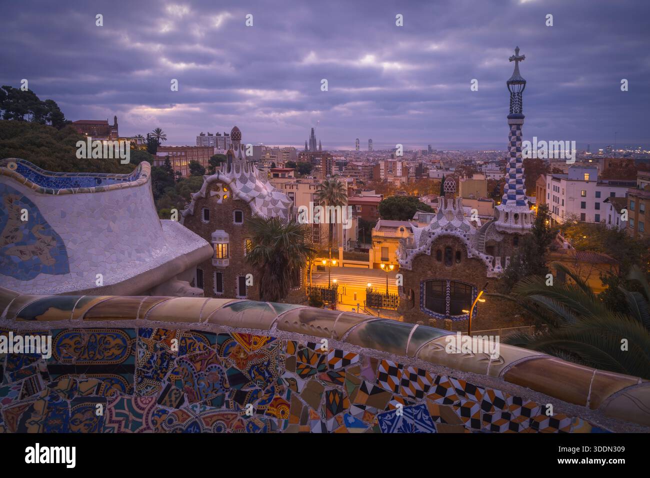 La lumière du matin baigne Park Guell dans des teintes douces, illuminant des mosaïques vibrantes tandis que la ville de Barcelone se réveille sous un ciel nuageux, en Catalogne Banque D'Images