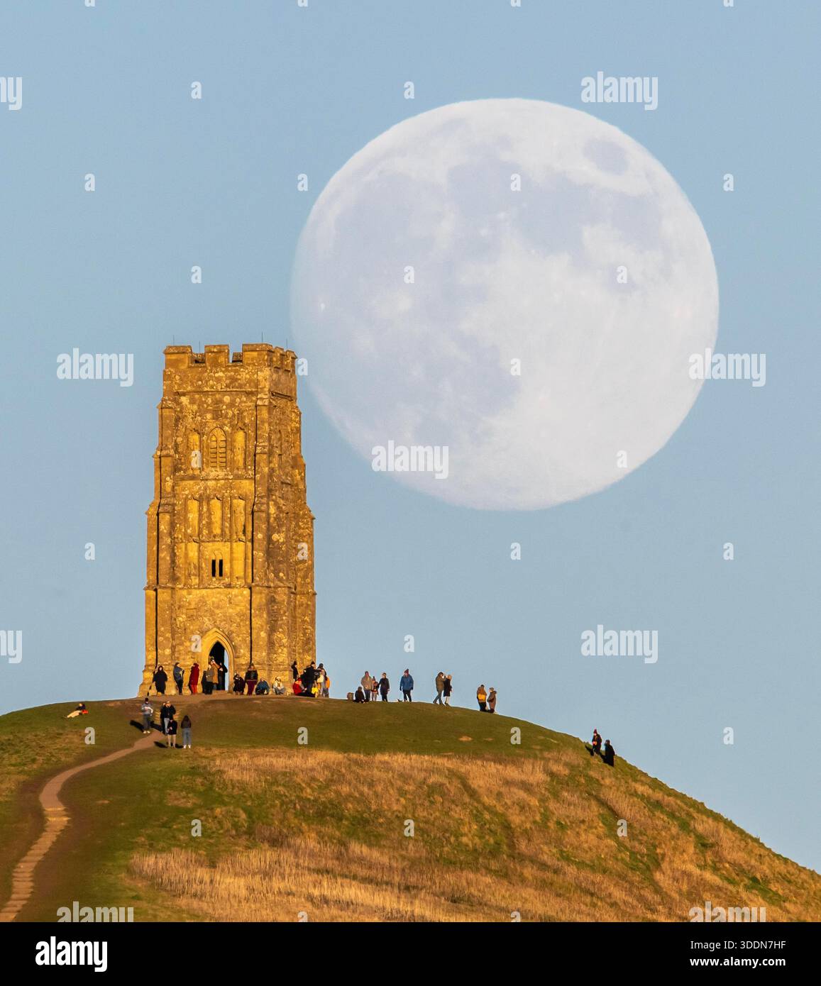 Glastonbury, Somerset, Royaume-Uni. 2 janvier 2026. Météo britannique. La lune presque pleine Wolf Moon se lève dans le ciel clair de l'après-midi de derrière la tour St Michael sur Glastonbury Tor à Glastonbury dans le Somerset comme une grande foule regarde. Ce mois la pleine lune est le 3 janvier sera une super lune. Crédit photo : Graham Hunt/Alamy Live News Banque D'Images