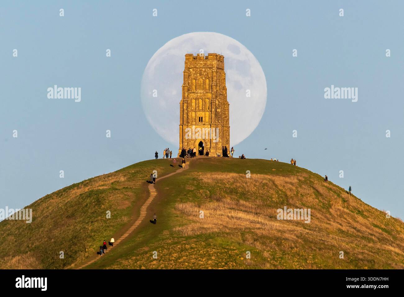 Glastonbury, Somerset, Royaume-Uni. 2 janvier 2026. Météo britannique. La lune presque pleine Wolf Moon se lève dans le ciel clair de l'après-midi de derrière la tour St Michael sur Glastonbury Tor à Glastonbury dans le Somerset comme une grande foule regarde. Ce mois la pleine lune est le 3 janvier sera une super lune. Crédit photo : Graham Hunt/Alamy Live News Banque D'Images