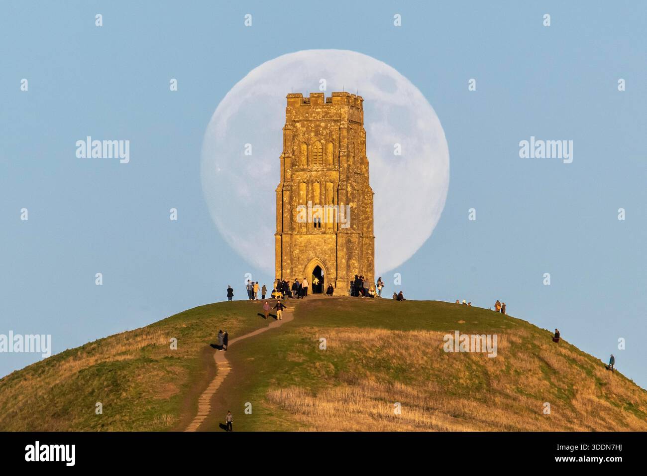 Glastonbury, Somerset, Royaume-Uni. 2 janvier 2026. Météo britannique. La lune presque pleine Wolf Moon se lève dans le ciel clair de l'après-midi de derrière la tour St Michael sur Glastonbury Tor à Glastonbury dans le Somerset comme une grande foule regarde. Ce mois la pleine lune est le 3 janvier sera une super lune. Crédit photo : Graham Hunt/Alamy Live News Banque D'Images