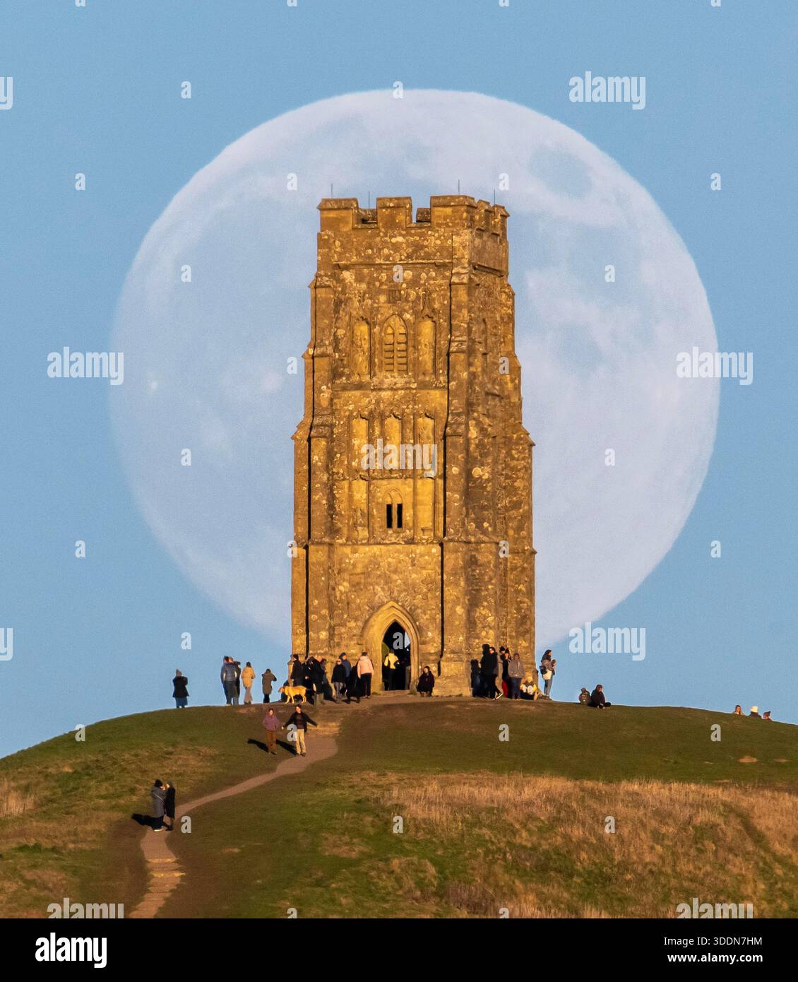 Glastonbury, Somerset, Royaume-Uni. 2 janvier 2026. Météo britannique. La lune presque pleine Wolf Moon se lève dans le ciel clair de l'après-midi de derrière la tour St Michael sur Glastonbury Tor à Glastonbury dans le Somerset comme une grande foule regarde. Ce mois la pleine lune est le 3 janvier sera une super lune. Crédit photo : Graham Hunt/Alamy Live News Banque D'Images