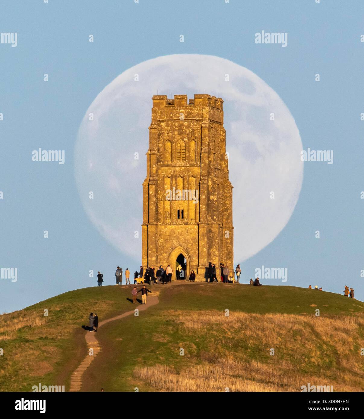 Glastonbury, Somerset, Royaume-Uni. 2 janvier 2026. Météo britannique. La lune presque pleine Wolf Moon se lève dans le ciel clair de l'après-midi de derrière la tour St Michael sur Glastonbury Tor à Glastonbury dans le Somerset comme une grande foule regarde. Ce mois la pleine lune est le 3 janvier sera une super lune. Crédit photo : Graham Hunt/Alamy Live News Banque D'Images