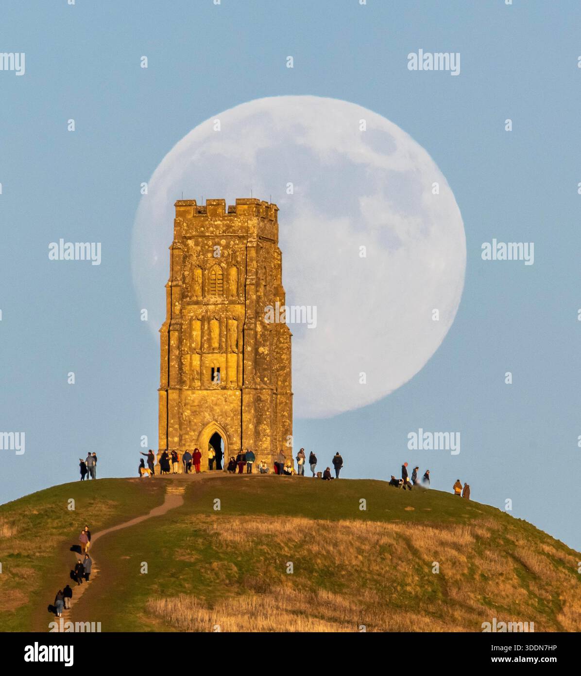 Glastonbury, Somerset, Royaume-Uni. 2 janvier 2026. Météo britannique. La lune presque pleine Wolf Moon se lève dans le ciel clair de l'après-midi de derrière la tour St Michael sur Glastonbury Tor à Glastonbury dans le Somerset comme une grande foule regarde. Ce mois la pleine lune est le 3 janvier sera une super lune. Crédit photo : Graham Hunt/Alamy Live News Banque D'Images