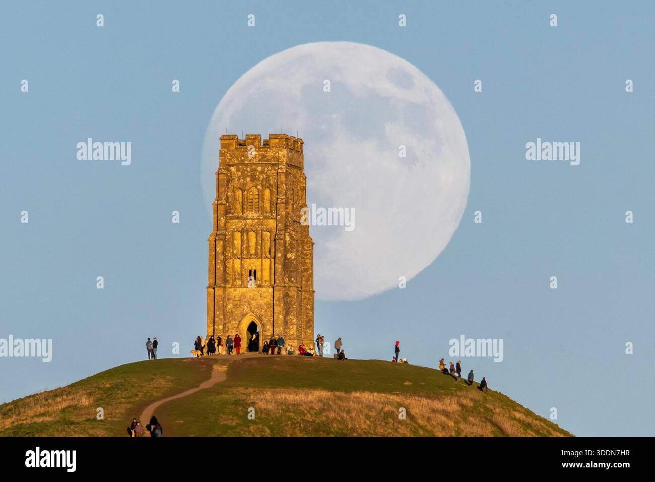Glastonbury, Somerset, Royaume-Uni. 2 janvier 2026. Météo britannique. La lune presque pleine Wolf Moon se lève dans le ciel clair de l'après-midi de derrière la tour St Michael sur Glastonbury Tor à Glastonbury dans le Somerset comme une grande foule regarde. Ce mois la pleine lune est le 3 janvier sera une super lune. Crédit photo : Graham Hunt/Alamy Live News Banque D'Images