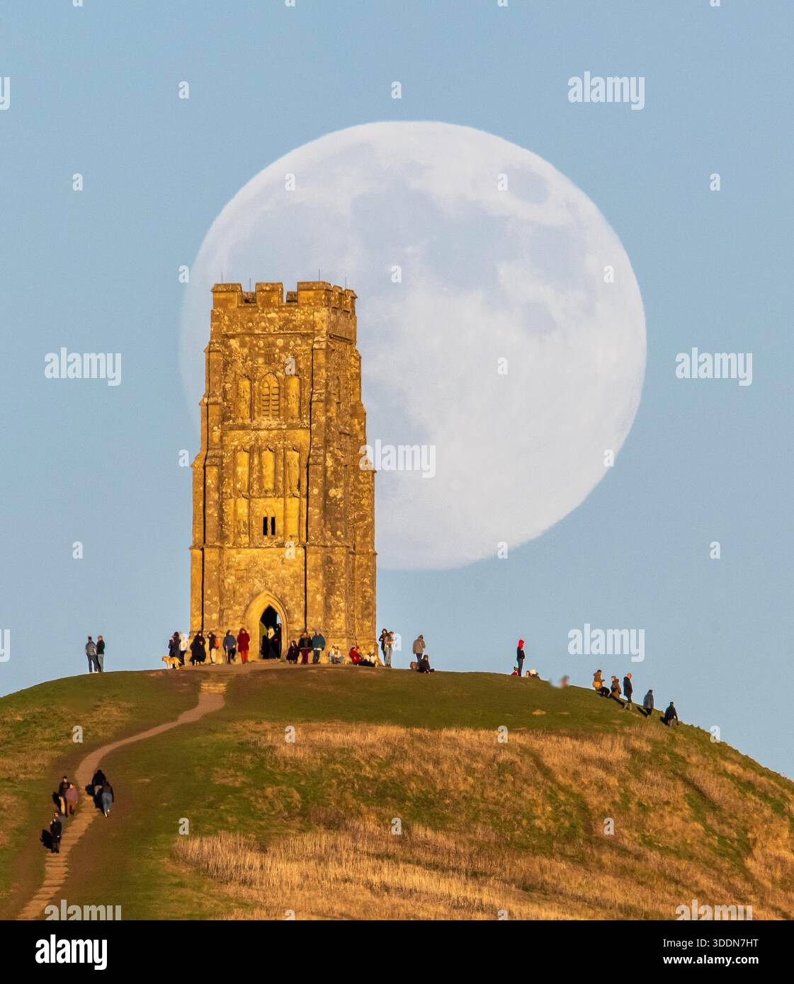 Glastonbury, Somerset, Royaume-Uni. 2 janvier 2026. Météo britannique. La lune presque pleine Wolf Moon se lève dans le ciel clair de l'après-midi de derrière la tour St Michael sur Glastonbury Tor à Glastonbury dans le Somerset comme une grande foule regarde. Ce mois la pleine lune est le 3 janvier sera une super lune. Crédit photo : Graham Hunt/Alamy Live News Banque D'Images