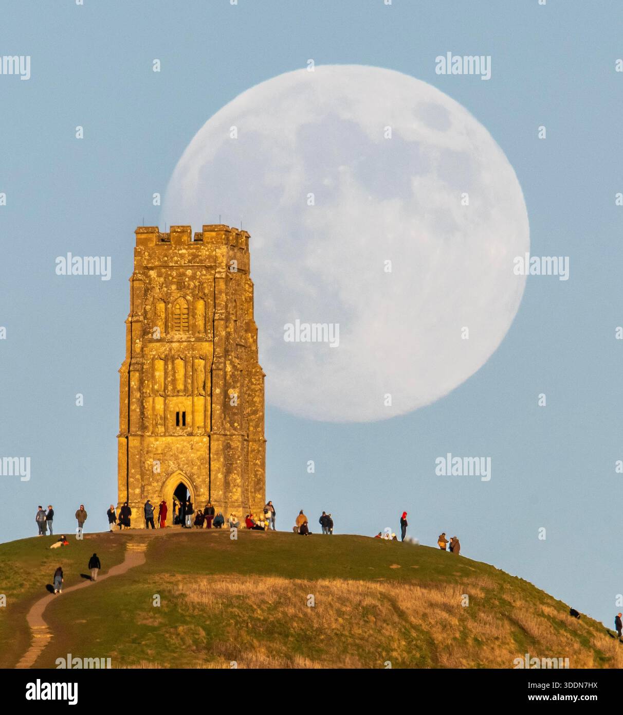 Glastonbury, Somerset, Royaume-Uni. 2 janvier 2026. Météo britannique. La lune presque pleine Wolf Moon se lève dans le ciel clair de l'après-midi de derrière la tour St Michael sur Glastonbury Tor à Glastonbury dans le Somerset comme une grande foule regarde. Ce mois la pleine lune est le 3 janvier sera une super lune. Crédit photo : Graham Hunt/Alamy Live News Banque D'Images