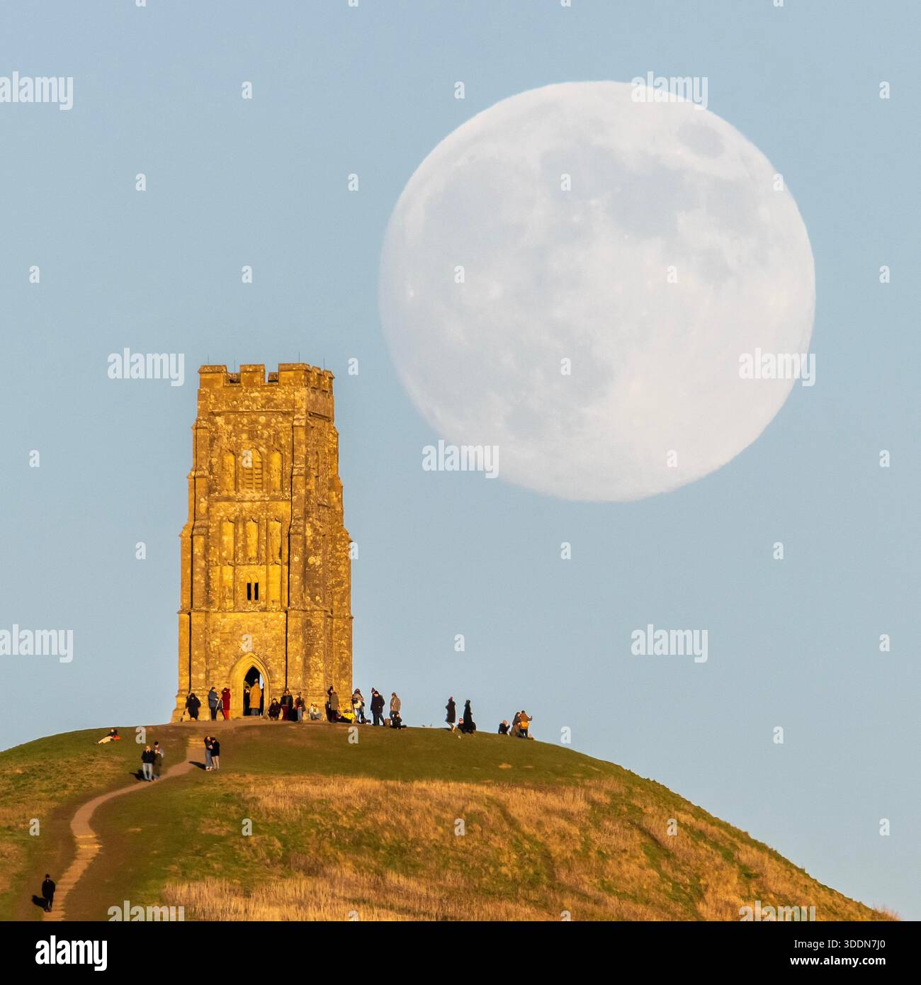 Glastonbury, Somerset, Royaume-Uni. 2 janvier 2026. Météo britannique. La lune presque pleine Wolf Moon se lève dans le ciel clair de l'après-midi de derrière la tour St Michael sur Glastonbury Tor à Glastonbury dans le Somerset comme une grande foule regarde. Ce mois la pleine lune est le 3 janvier sera une super lune. Crédit photo : Graham Hunt/Alamy Live News Banque D'Images