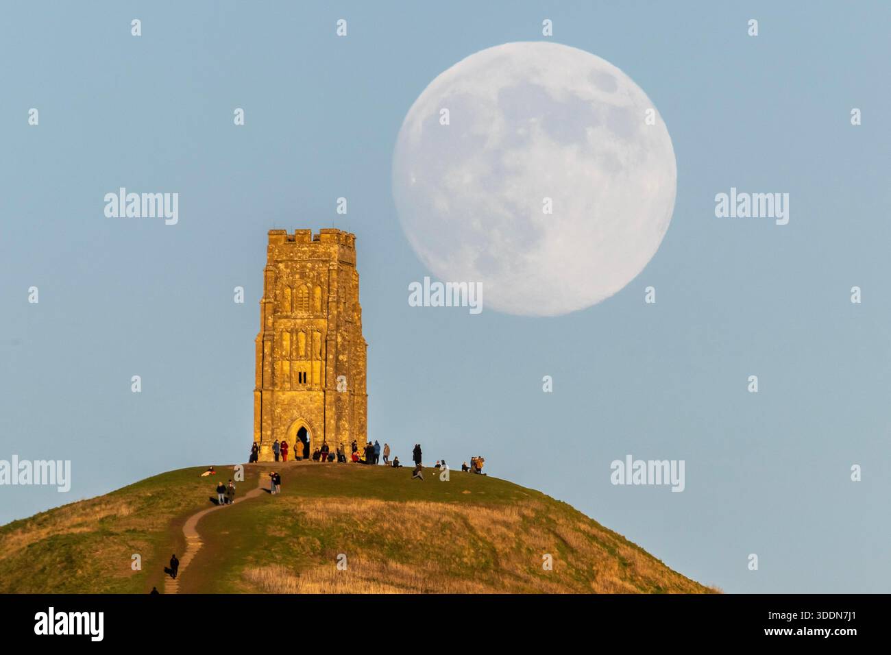 Glastonbury, Somerset, Royaume-Uni. 2 janvier 2026. Météo britannique. La lune presque pleine Wolf Moon se lève dans le ciel clair de l'après-midi de derrière la tour St Michael sur Glastonbury Tor à Glastonbury dans le Somerset comme une grande foule regarde. Ce mois la pleine lune est le 3 janvier sera une super lune. Crédit photo : Graham Hunt/Alamy Live News Banque D'Images